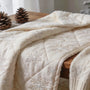 Cozy winter quilt with snowflake patterns on a wooden table surrounded by winter decor, reflecting warmth and creativity.