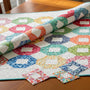 Colorful charm square quilt on a wooden table, showcasing various fabric patterns